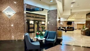 Eine Lobby mit einer Rezeption, einer Sitzecke mit Sesseln und einer Pflanzengruppe.