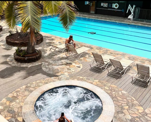 A swimming pool with lounge chairs, a hot tub, and a palm tree.