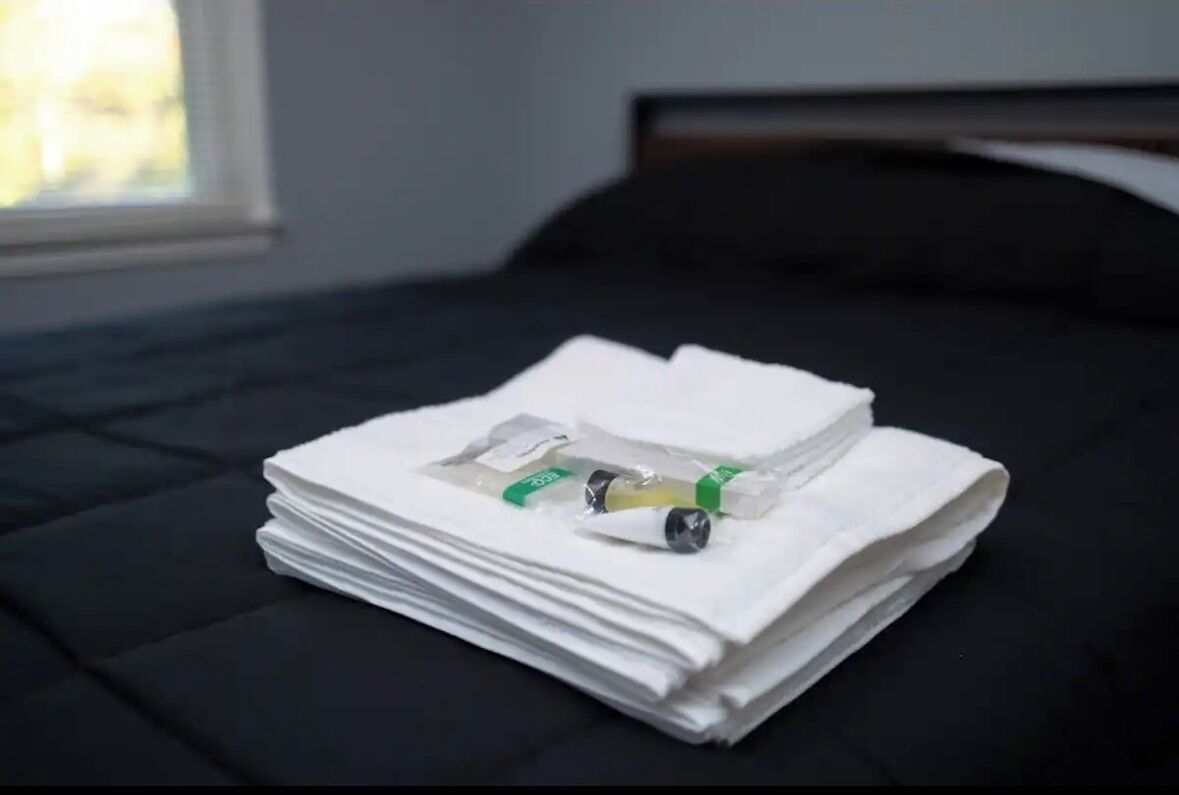 A neatly folded stack of white towels on a black bed with a window in the background.