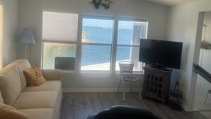 A living room with a TV, a ceiling fan, a window with a view of the sea, a sofa, and a chair. - Cozy 2-bedroom home in beautiful Palmetto with spectacular waterfront views. (Palmetto)