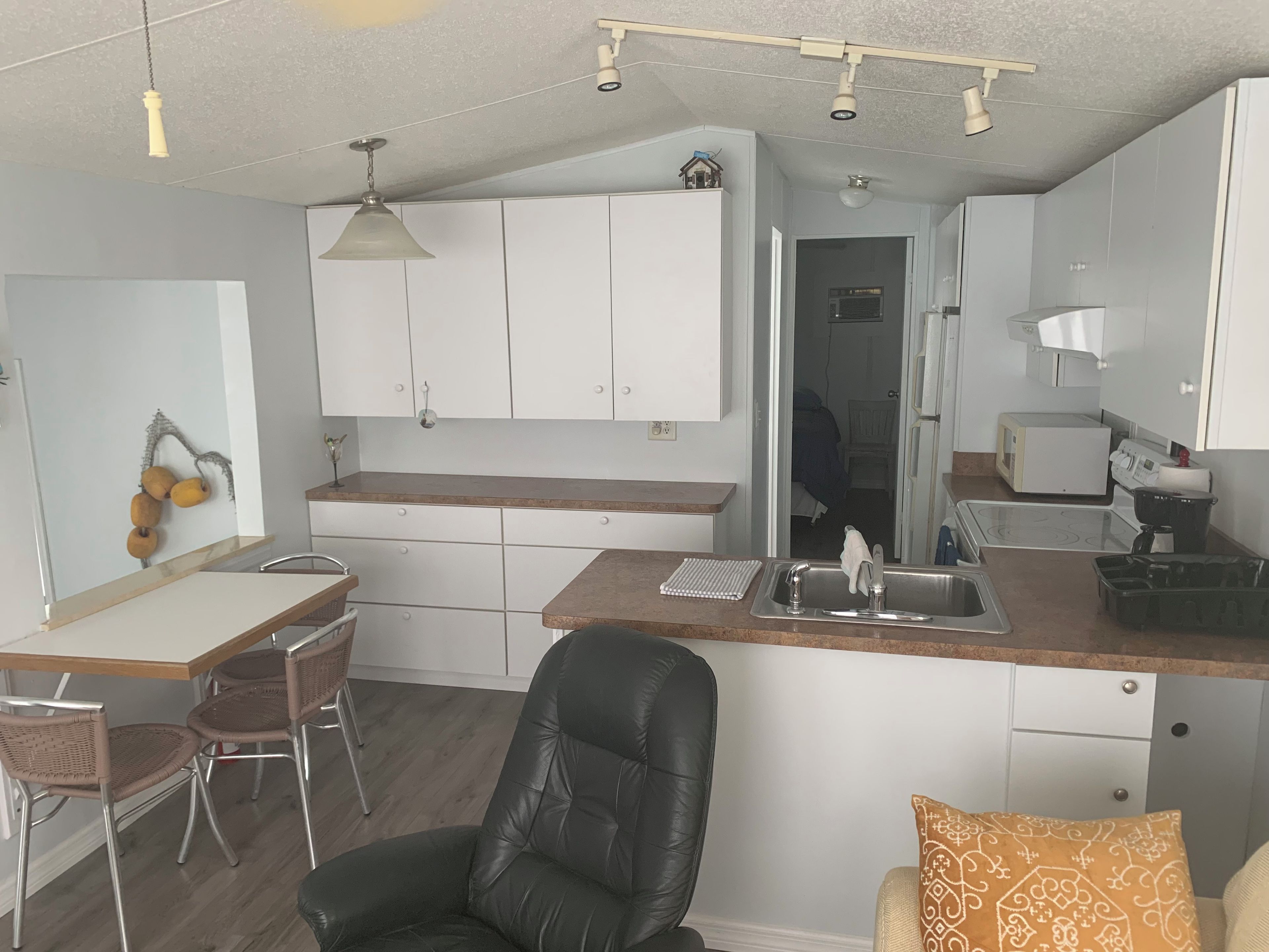 A compact kitchen with white cabinets, a wooden countertop, and a black leather chair.