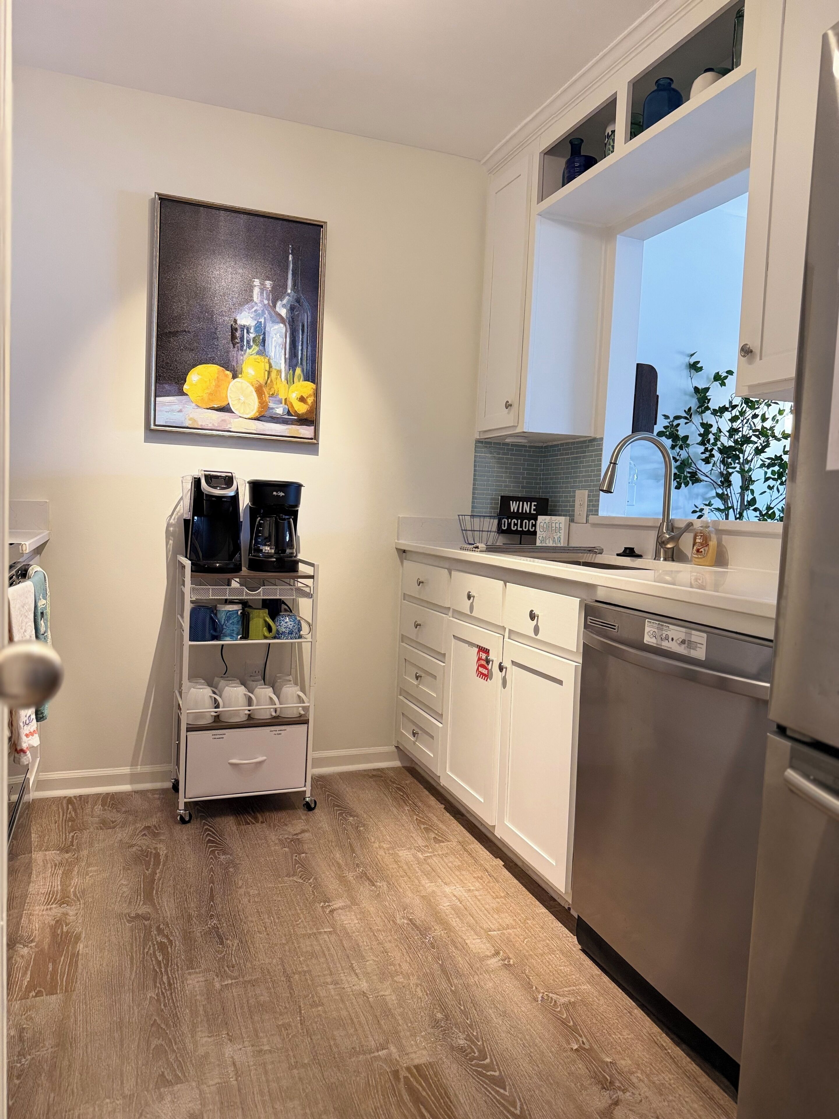 A kitchen with a coffee maker, a dishwasher, and a window with a view of the outside.