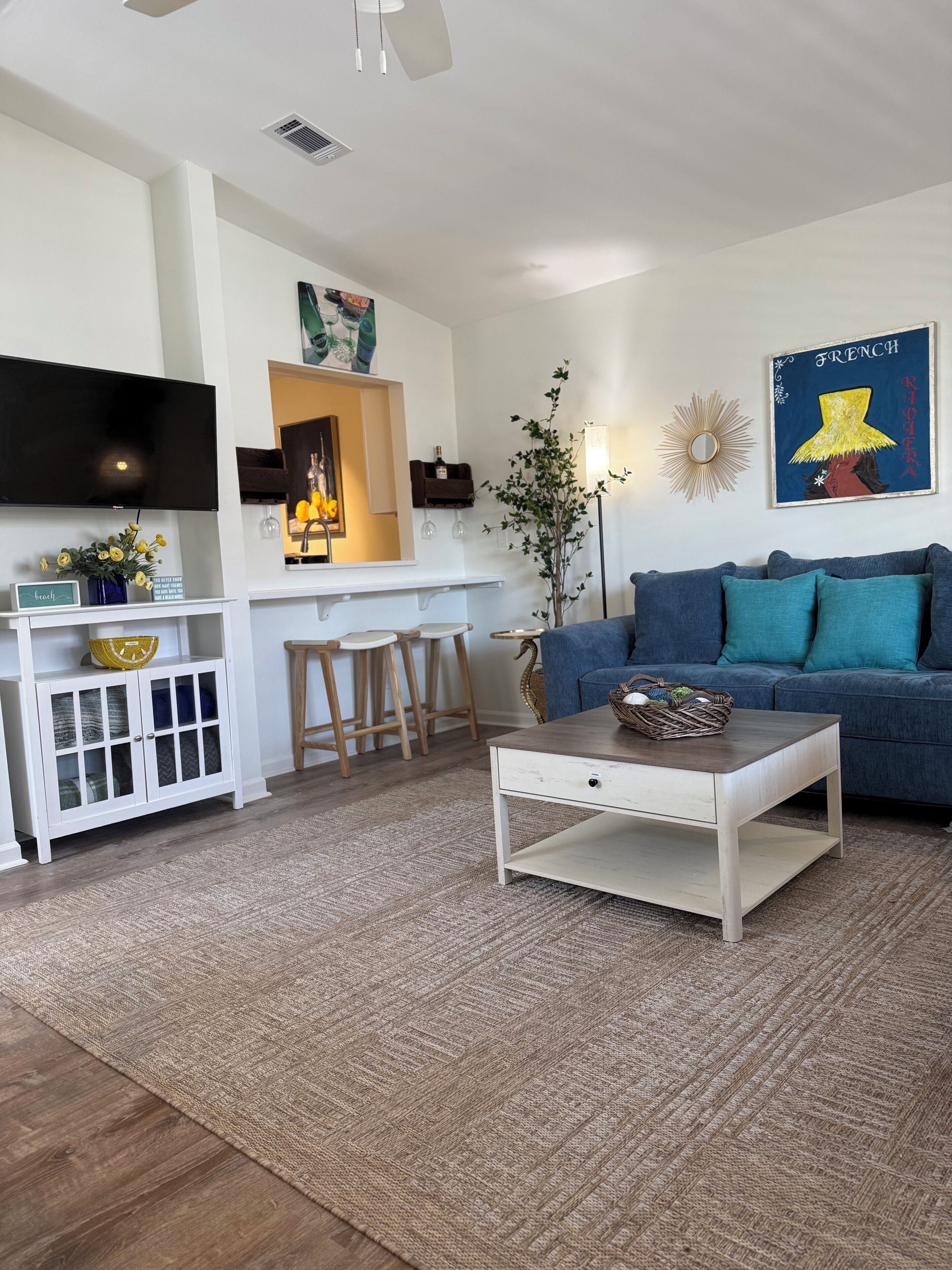 A modern living room with a TV, sofa, coffee table, and a kitchen area with stools.