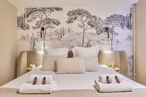 Quarto de hotel com cama, almofadas, mesa de cabeceira e um mural na parede.
