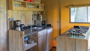 A compact kitchen with wooden cabinetry, a gas stove, a microwave, and shelves with dishes and utensils.