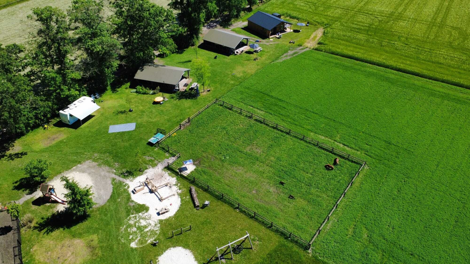An aerial view of a property with a fenced field, a small building, and a trailer.