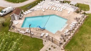 Une vue aérienne d’une piscine rectangulaire avec un toboggan bleu, entourée de chaises longues et d’un petit abri de jardin.