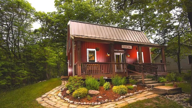 Un chalet rustique doté d’un porche en bois, d’un escalier menant à l’entrée et d’un jardin bien entretenu.