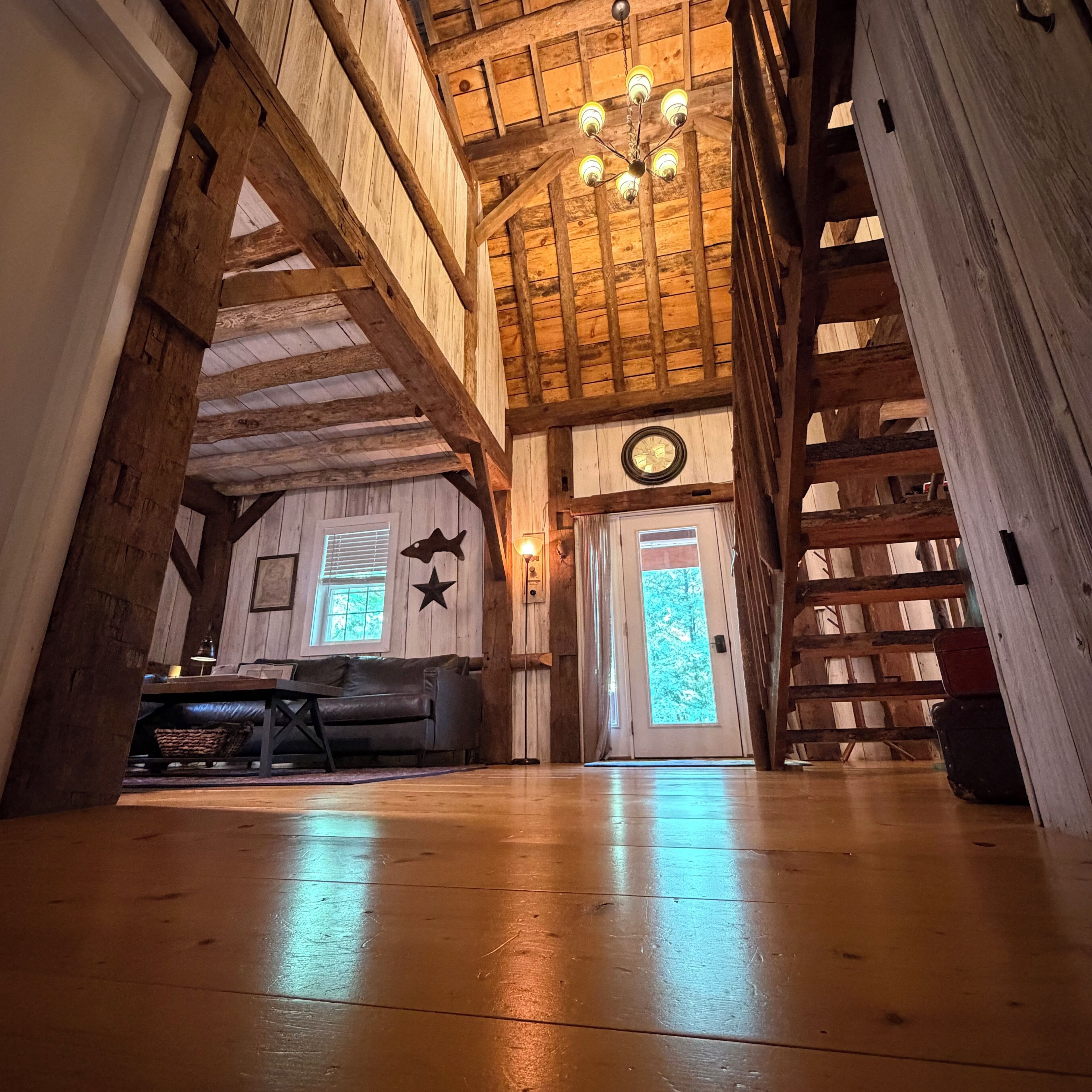 A spacious room with a wooden ceiling, a chandelier, a fireplace, and a large window.