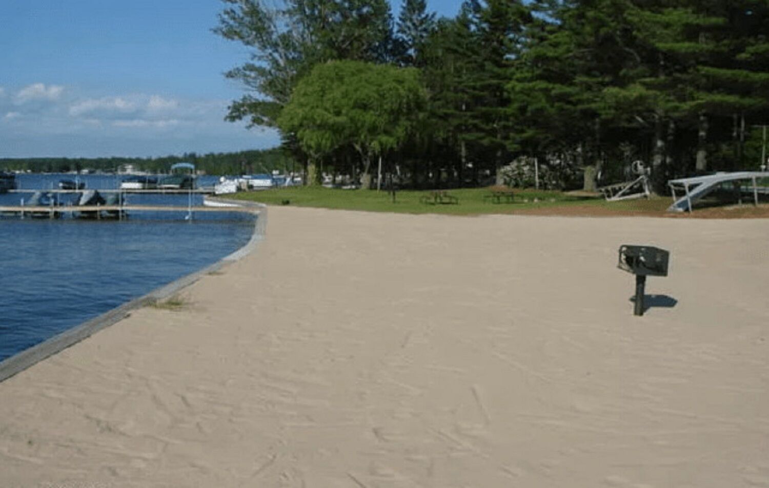 A sandy beach with a mailbox and a dock with boats.