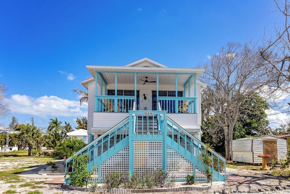A two-story building with a blue staircase leading to the entrance, surrounded by greenery and a clear sky.