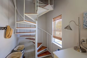 A spiral staircase with wooden steps and white railings, a window with bamboo blinds, a woven basket, and a desk lamp.