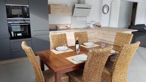 Uma cozinha moderna com eletrodomésticos embutidos, um espaço de jantar com cadeiras de vime e um relógio na parede.