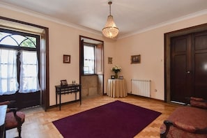 A room with wooden flooring, a purple rug, a chandelier, a door, and a window with curtains.