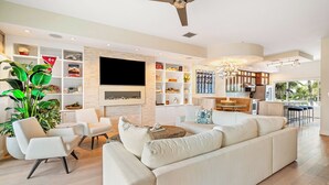 Ein modernes Wohnzimmer mit Sofa, Sesseln, einem Fernseher und einer Küche im Hintergrund.