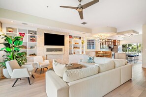 A modern living room with a sofa, chairs, a TV, and a kitchen in the background. - Pass A Grille Don Cesar Pool Boat Slip 3/3.5 (St Pete Beach)