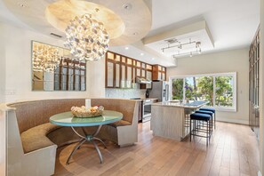 A modern kitchen with a central island, a dining area with a glass table, and a large window with a view of greenery. - Pass A Grille Don Cesar Pool Boat Slip 3/3.5 (St Pete Beach)