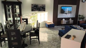 A modern living room with a dining area, a TV mounted on the wall, and a potted plant. - Djerba Aldo Piscine  (Houmt Souk)