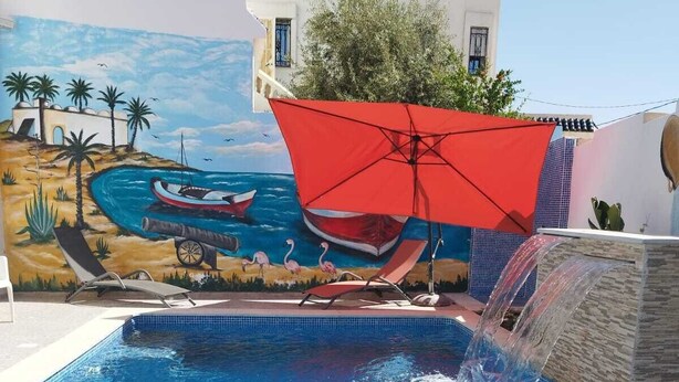A swimming pool with a mural, a red umbrella, and a waterfall feature. - Djerba Aldo Piscine  (Houmt Souk)