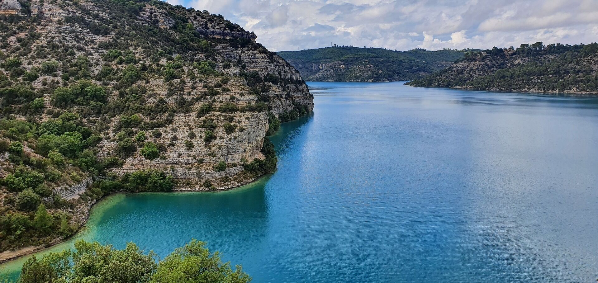 A coastal landscape with a clear blue lake, rocky cliffs, and dense greenery.