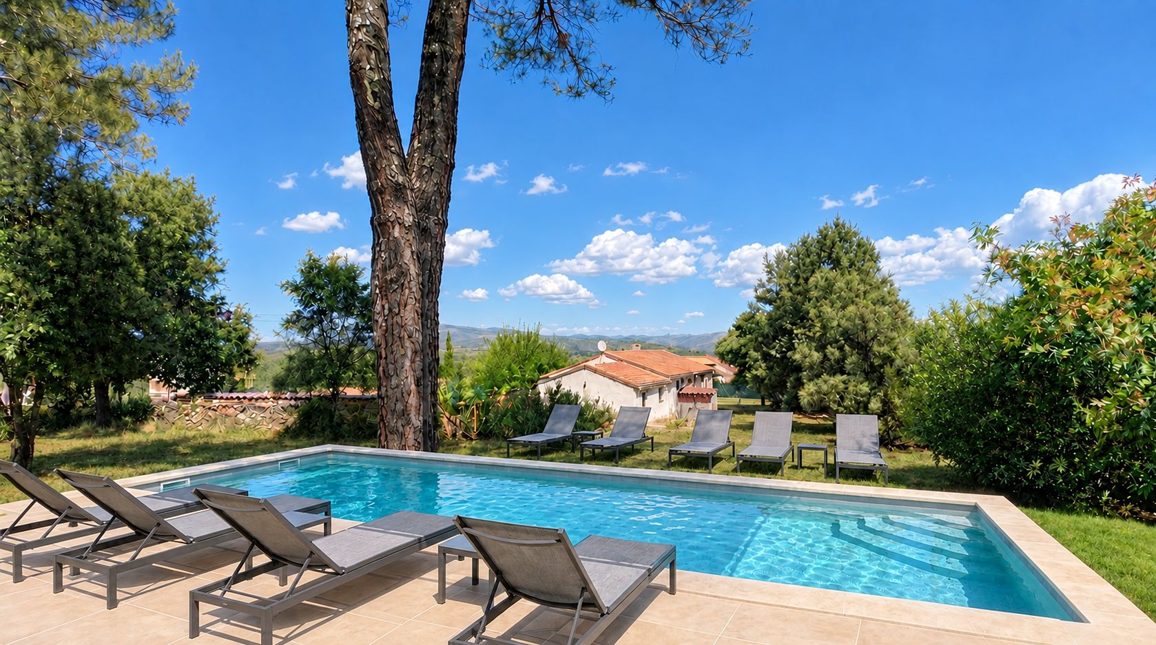 A swimming pool with lounge chairs, surrounded by trees and a view of a house.