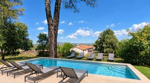 Une piscine entourée d’arbres, avec des chaises longues et une vue sur une maison.
