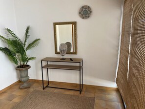 Une pièce comprenant une console en bois, une plante en pot, un miroir et un panneau mural texturé.