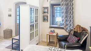 Una stanza con un'ampia porta ad arco, una finestra con tenda, una poltrona in pelle, un tavolino con una lampada e quadri appesi al muro.