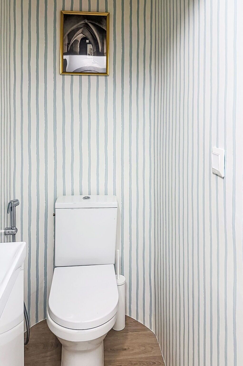 A bathroom with a striped wall, a toilet, a bidet, and a small framed picture above the toilet.
