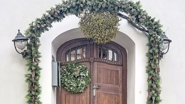 Una porta in legno decorata con un'ghirlanda, piante in vaso e un lanterna sui gradini.