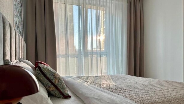 Ein Hotelzimmer mit Bett, Vorhängen, einer Lampe und Blick ins Freie.