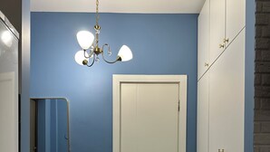 Ein Flur mit einer weißen Tür, einem roten Pouf, einer Chandelüster und einem Kleiderschrank mit goldfarbenen Griffen.