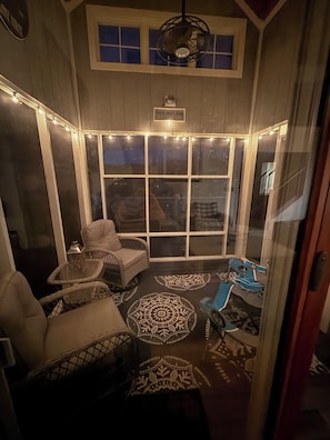 A covered patio area with wicker furniture, a patterned rug, and string lights.
