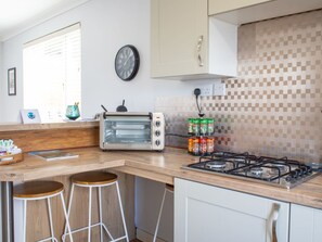 Een keuken met een ingebouwde toasteroven, een gasfornuis, een wandklok en een raam met jaloezieën.