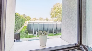 Uma janela com vista para um edifício, um vaso com planta e uma área gramada.