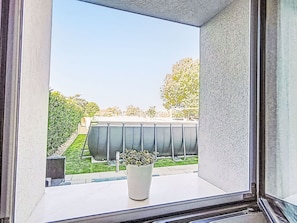 Una finestra con vista su un edificio, una pianta in vaso e una zona verde.