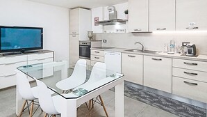 Uma cozinha moderna com armários brancos, uma mesa de jantar de vidro e um forno embutido.