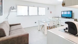 Uma sala de estar moderna com sofá, mesa de jantar de vidro, televisão e abajur.