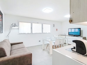 Un soggiorno moderno con un divano, un tavolo da pranzo in vetro, una TV e una lampada.