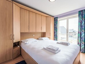 Un dormitorio con una cama grande, un armario de madera y una ventana con vistas a edificios.