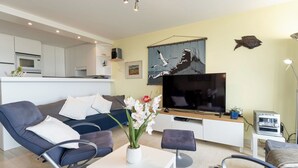 Ein modernes Wohnzimmer mit Sofa, Couchtisch, Fernseher und einer Küche im Hintergrund.