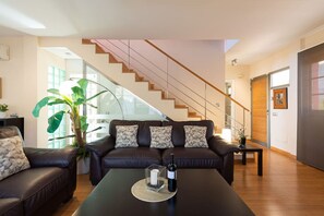 A modern living room with a sofa, a coffee table with a bottle, a staircase, and a large plant. - Villa del Sur - Luxury with heated pool and BBQ (Mogán)