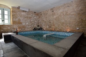 Ein Zimmer mit Steinwänden, einem gefliesten Pool, einer Steinsitzbank und einem kleinen Tisch mit einer Flasche und Gläsern.