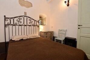 A bedroom with a metal bed frame, a wooden dresser, a chair, and a wall-mounted lamp. - Private Villa with WIFI, private pool, A/C, hot tub, TV, terrace, pets allowed, panoramic view (Chiaramonte Gulfi)