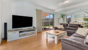 Een moderne woonkamer met een flatscreen televisie, een leren bank en een eethoek met een tafel en stoelen.
