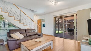 Een moderne woonkamer met een trap, een bank, een salontafel en een glazen schuifdeur naar een buitenruimte.