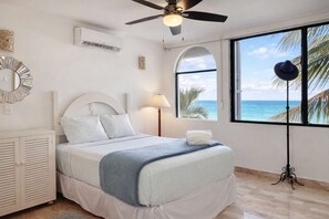 A bedroom with a bed, a ceiling fan, a window with a view of the ocean, and a wall-mounted air conditioner. - Oceanfront 2BR - Cancun - Beach Access - Sleeps 6 (Cancún)
