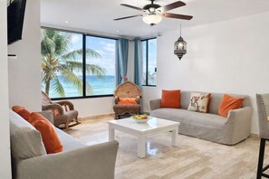 A living room with a view of the ocean, a ceiling fan, a white coffee table, and wicker furniture. - Oceanfront 2BR - Cancun - Beach Access - Sleeps 6 (Cancún)