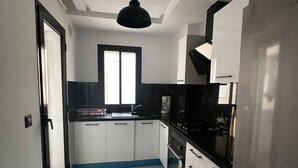 Μια σύγχρονη κουζίνα με λευκά ντουλάπια, έναν μαύρο πάγκο, ένα παράθυρο και ένα ψυγείο από ανοξείδωτο ατσάλι.