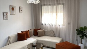Ένα μοντέρνο σαλόνι με έναν καναπέ, ένα οθωμανικό, ένα τραπεζάκι σαλονιού και ένα φωτιστικό οροφής.